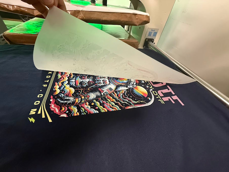 Kick DTF transfer being peeled hot from a shirt